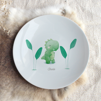 Assiette en porcelaine dinosaure (vert) avec végétation sur les côtés et prénom personnalisable.
