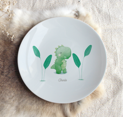 Assiette en porcelaine dinosaure (vert) avec végétation sur les côtés et prénom personnalisable.