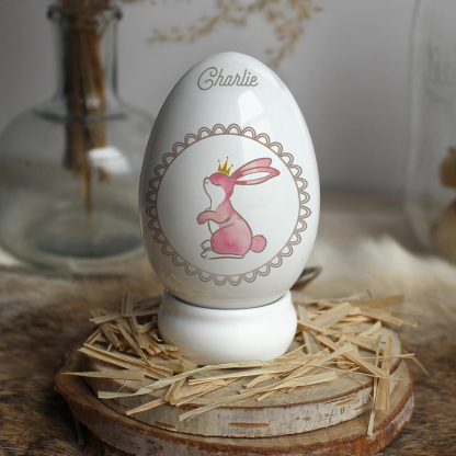 Œuf en porcelaine lapin rose entouré par un cercle effet dentelle avec prénom personnalisable.